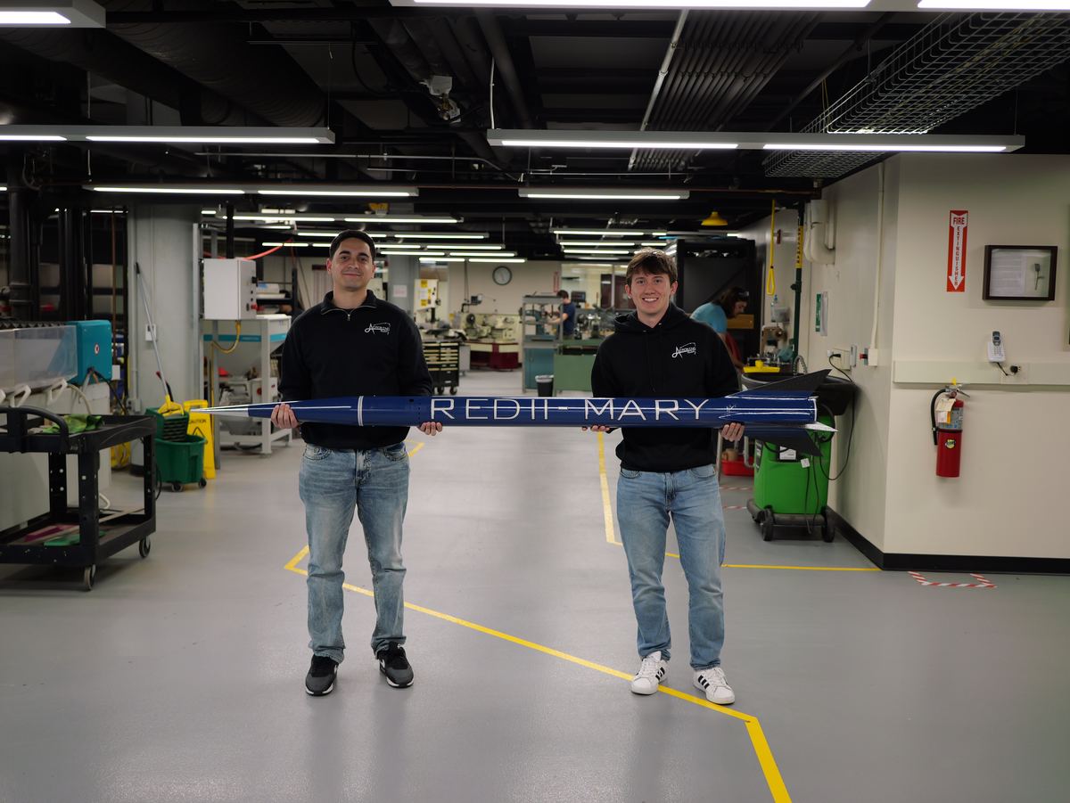 Two AeroBing members holding the assembled RED II Mary airframe horizontally in the machine shop.
