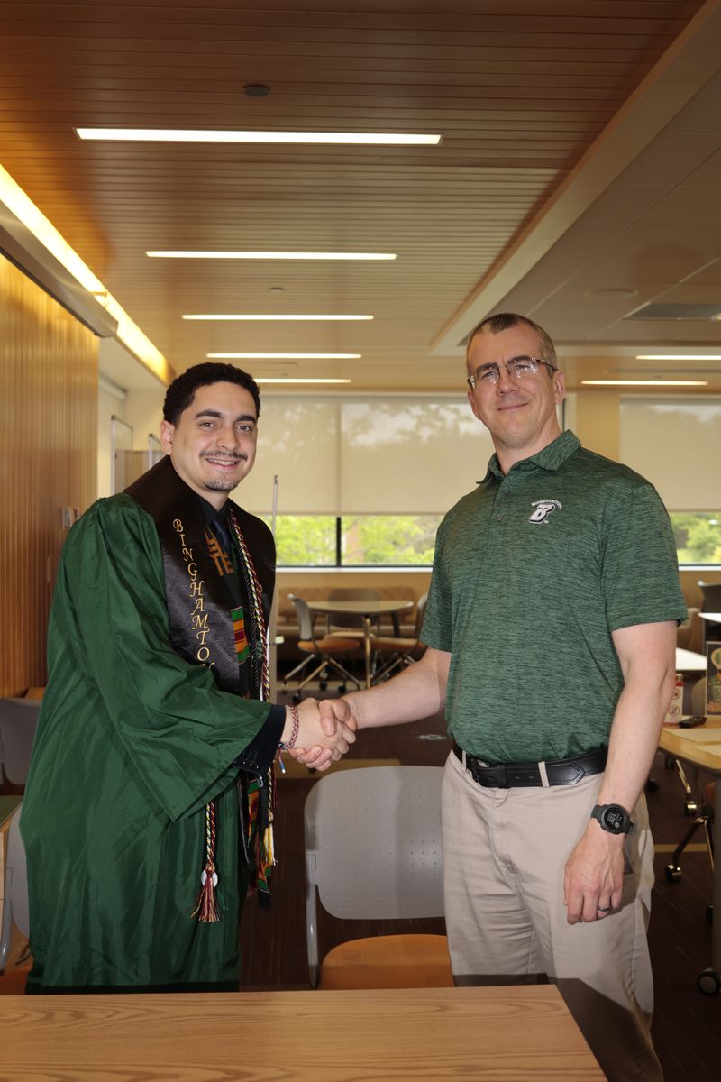 Kevin Polanco in graduation regalia shaking hands with his supervisor at the tutorial center.