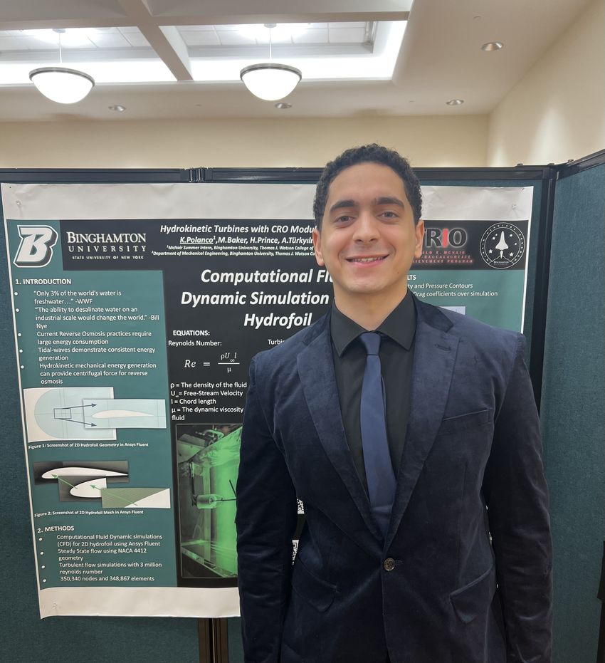 Kevin Polanco standing beside his research poster on computational fluid dynamic simulation of a hydrofoil for hydrokinetic turbines with a CRO module.